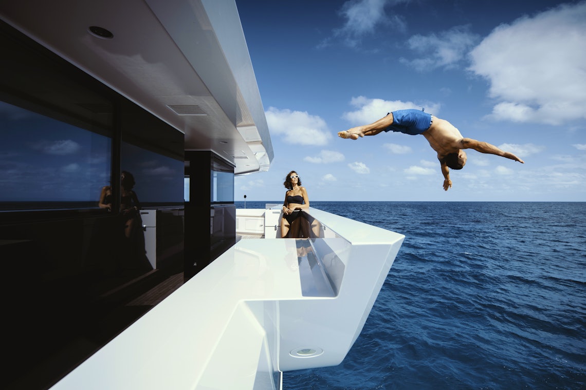 Woman Watches as a Man Dives Backwards into a Blue Ocean off a Yacht