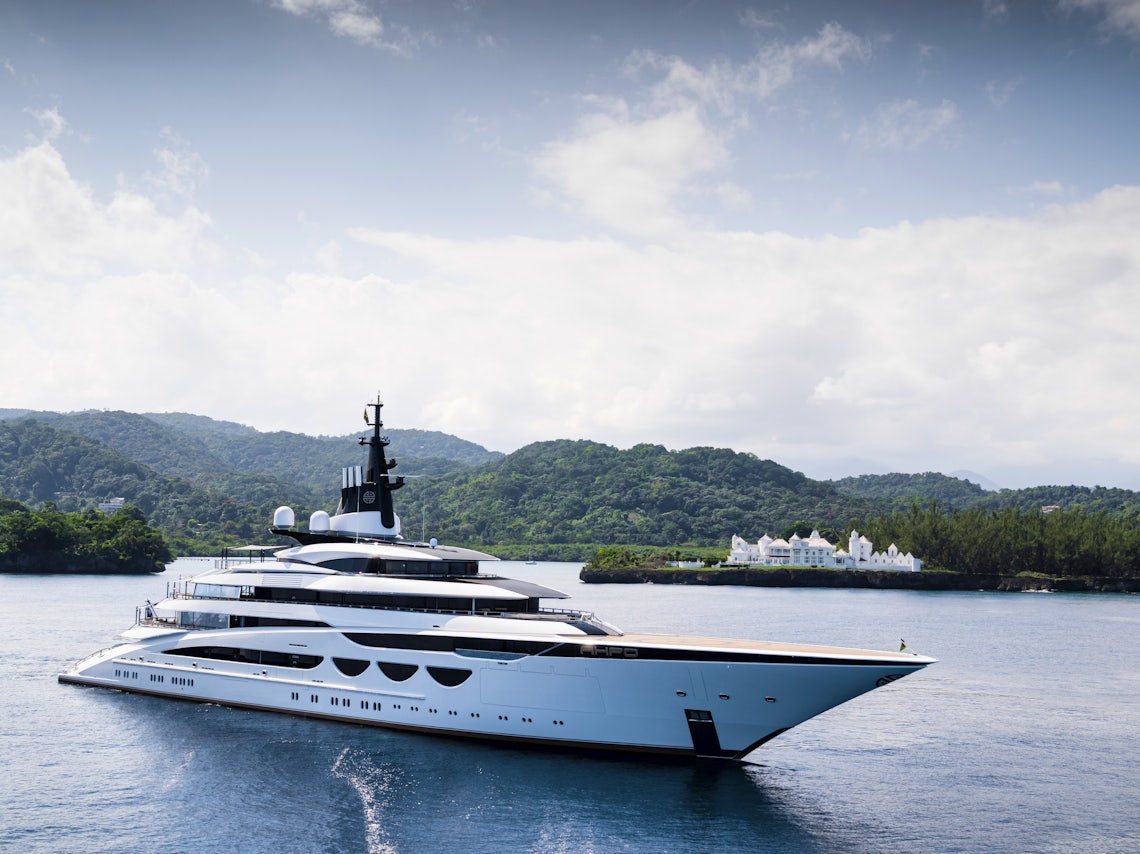 Yacht on Open Water with Green Mountains in the Background and a Cloudy Sky
